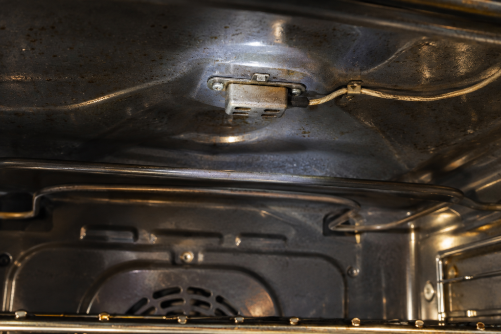 A small humidity sensor on the arched ceiling of an oven cavity with a light grease film on its housing.